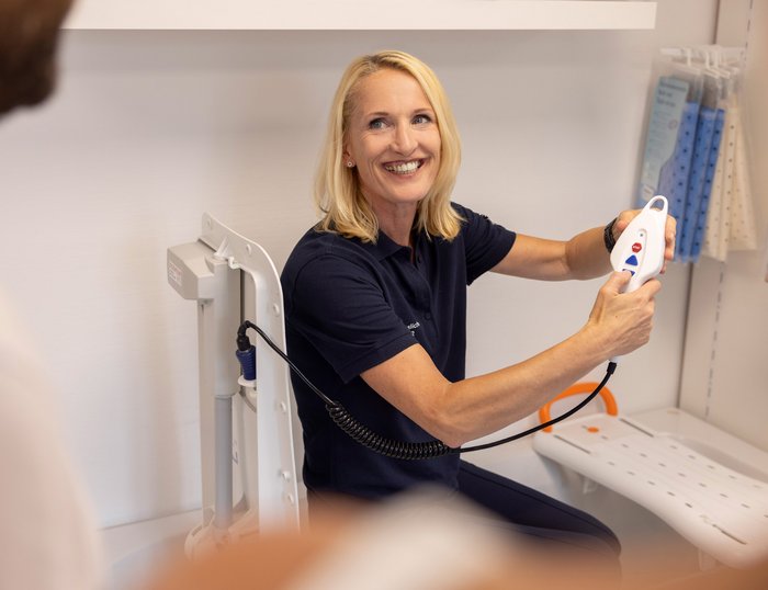 Geräteberatung durch MOT-Mitarbeiterin MOT-Mitarbeiterin zeigt einem Kunden die Funktion eines medizinischen Geräts und erklärt die Bedienung