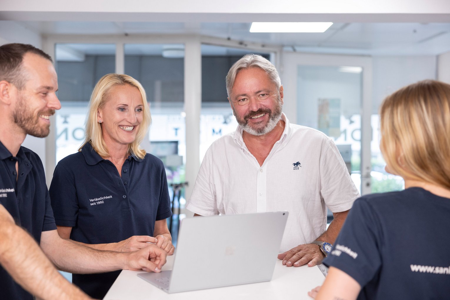 Teammeeting bei MOT Sanitätshaus Vier MOT-Mitarbeitende stehen zusammen um einen Tisch und besprechen etwas am Laptop in freundlicher Atmosphäre